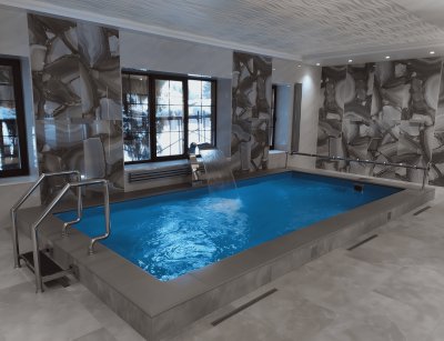 Крытый бассейн с голубой водой, лестницей и плиткой из серо-бежевого камня